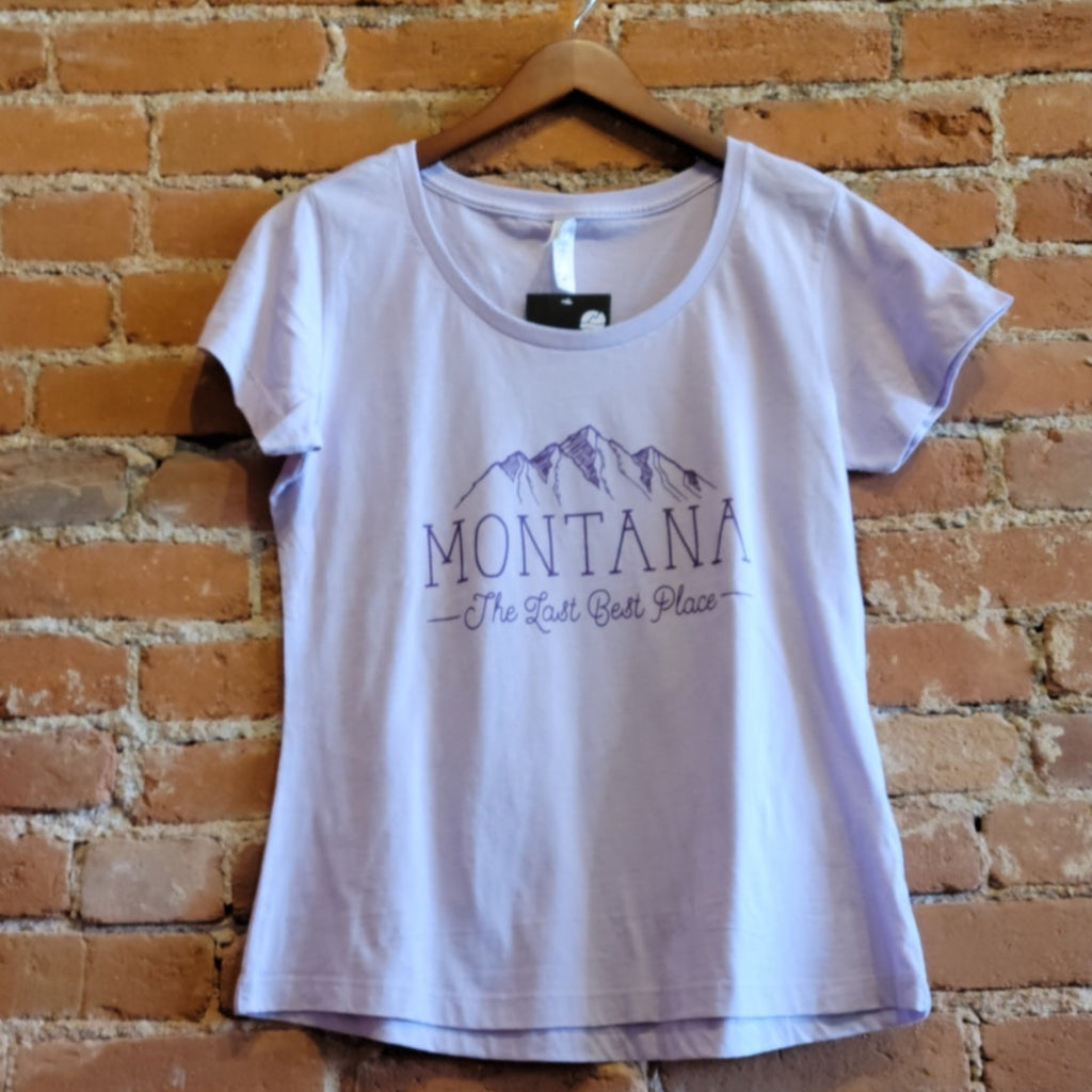 Front of Ouray women's scoop neck, short sleeve tee in the colorway Desert Sage (light purple). The logo is printed in an dark purple color depicting mountains above the text "Montana, The Last Best Place."