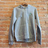 Front of Ouray women's hoody, drawstrings match the Premium Heather (light grey) colorway of the hoody. There are thumbholes, a kangaroo pocket and zipper down the front.  There is  an embroidered "Montana" logo under blue mountains.