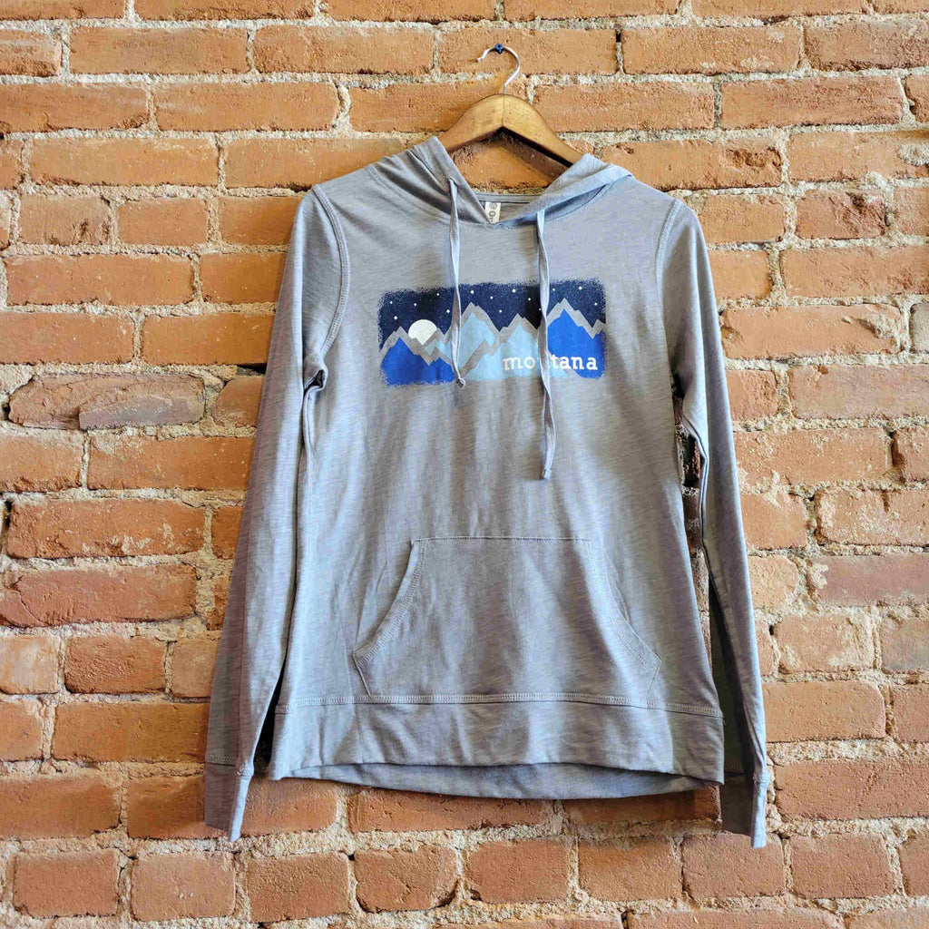 Picture of Ouray women's lightweight hoody in the colorway Medium Grey Heather (light grey). The front features jersey drawstrings, thumbholes, and a kangaroo pocket.  The print depicts a blue mountain range with a starry night sky. "Montana" is printed on the bottom right corner of the image.