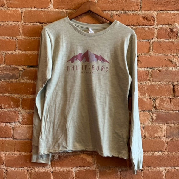 Front of the Ouray women's long sleeve shirt in the colorway Desert Sage (light green). The Print on the from consists of purple snowy mountains and the text "Philipsburg Montana". 